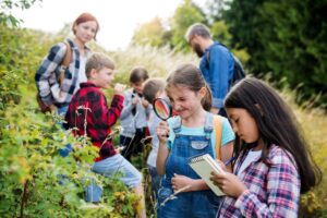 Children outside using magnifying glass and journaling