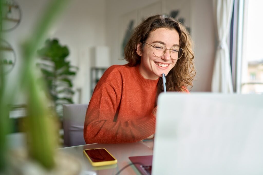Woman wearing orange/red sweater smiling while looking at her computer