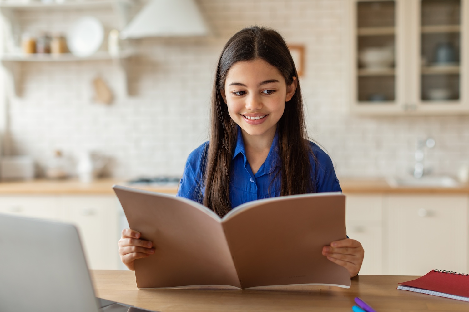 Little girl sitting in kitchen smiling while reading packet of information