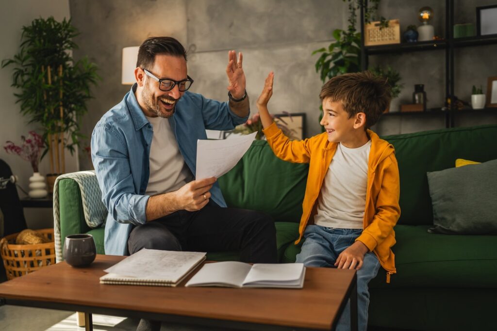 Father and son sitting on a green couch high-fiving