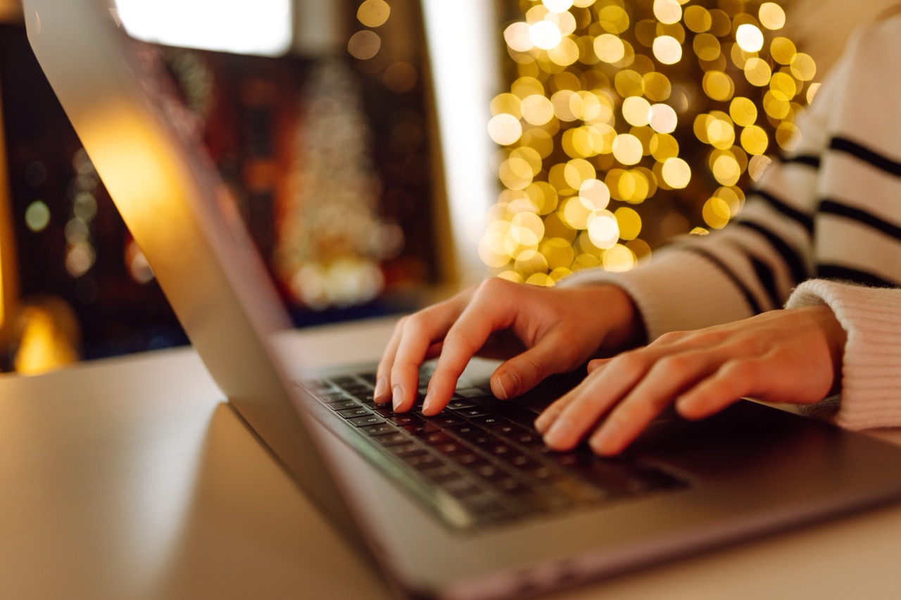 Child typing on a computer in front of a christmas tree.