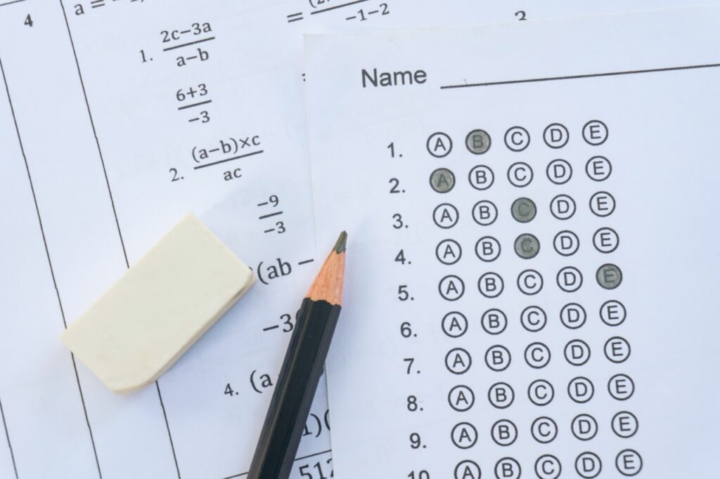 A multiple choice answer sheet and math worksheet laid on a flat surface next to a pencil and eraser, representing student state testing preparation.