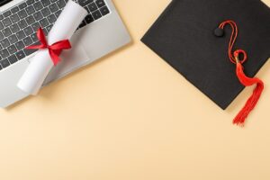 Graduation items, including a cap with a tassel, diploma, and a laptop, arranged